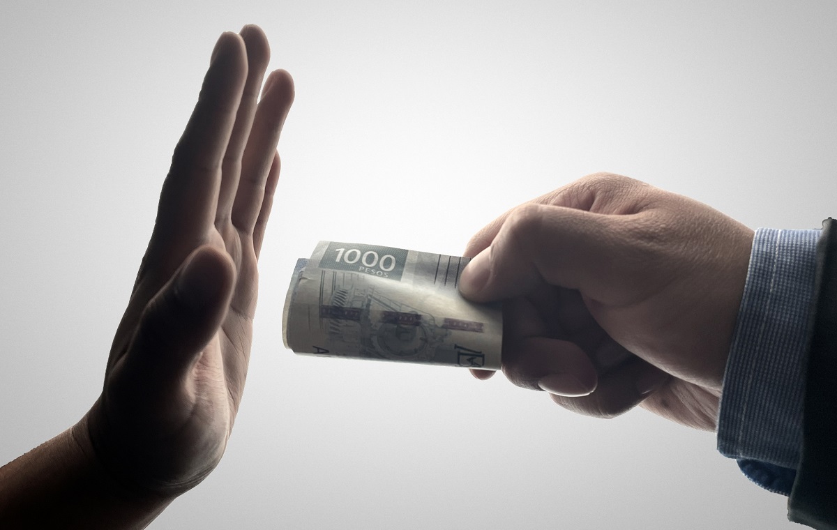Slika prikazuje eno roko, ki daje zvitek denarja, in drugo roko, ki zavrača denar.