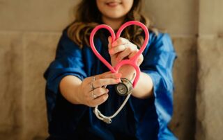 Slika prikazuje žensko z rjavimi lasmi, ki v rokah drži plastično srce in stetoskop.