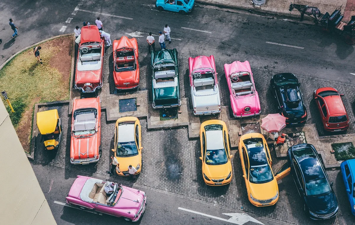 Slika prikazuje parkirišče z roza in rumenimi taksi avtomobili v New York stilu.