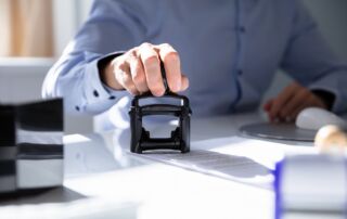 Slika prikazuje uradno osebo, ki v rokah drži žig na dokumentaciji.