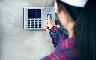 Slika prikazuje zaposleno žensko s kapo, ki s prstnim odtisom označi svoj prihod na delovno mesto.