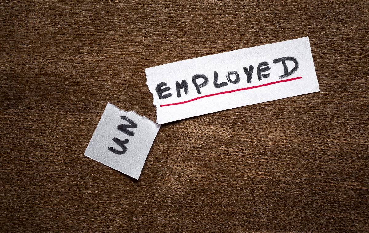 Slika prikazuje list papirja, na katerem piše Unemployed. List je raztrgan pri preponi Un. List je na rjavi leseni podlagi.