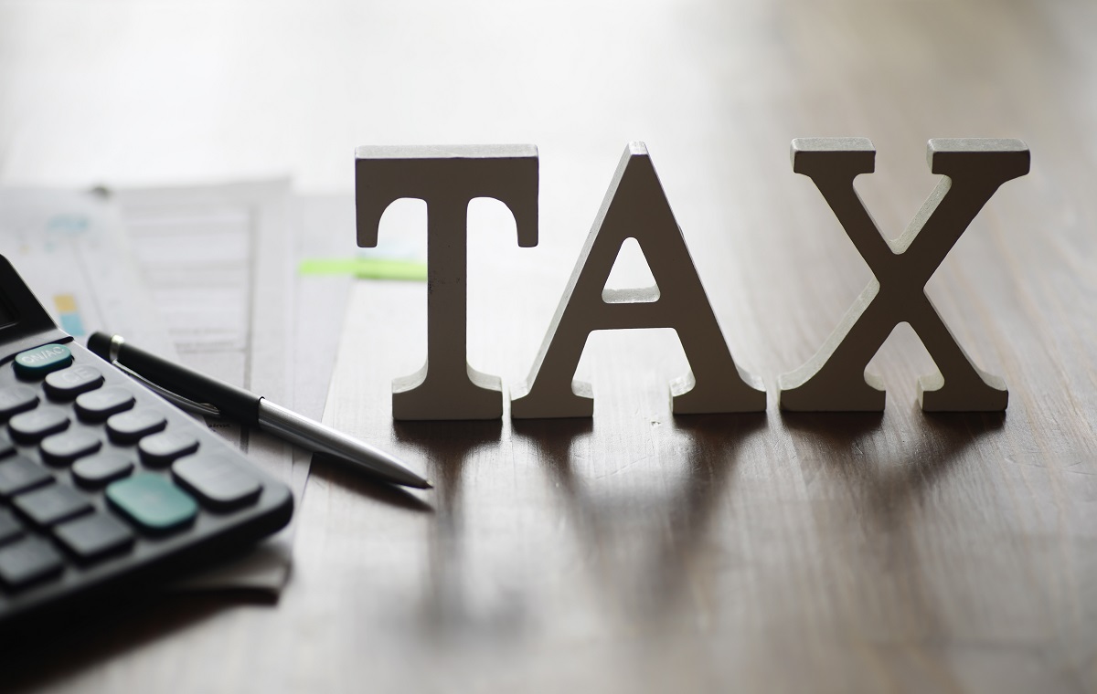 Slika prikazuje besedo TAX ter pisalo in kalkulator na sivi podlagi.