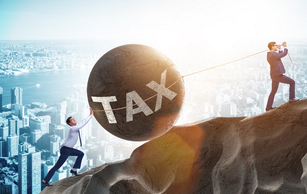 Dve moški osebi, ki vlečeta in potiskata veliko kroglom na kateri piše TAX, po hribu navzgor.