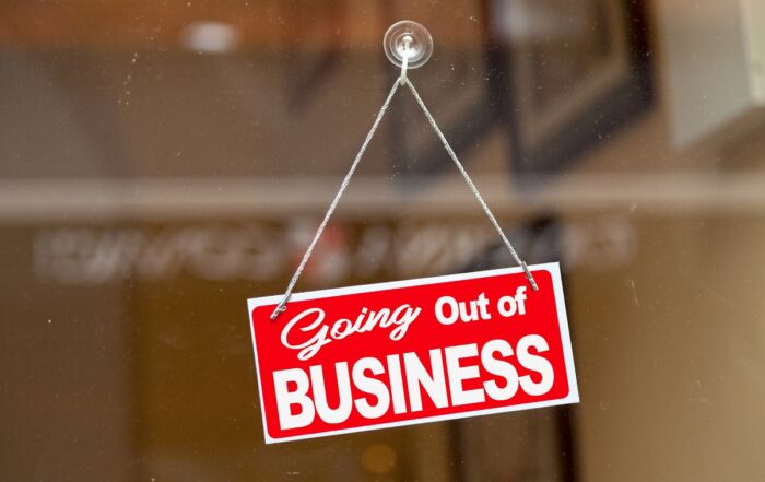 Slika prikazuje rdeč znak, ki visi na steklenih vratih trgovine z napisom Going Out of Business oz. zapiramo poslovanje.